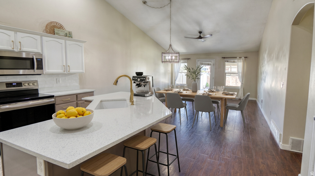 Kitchen island with a built-in sink and gold-finish faucet, white upper cabinetry, and stainless steel appliances