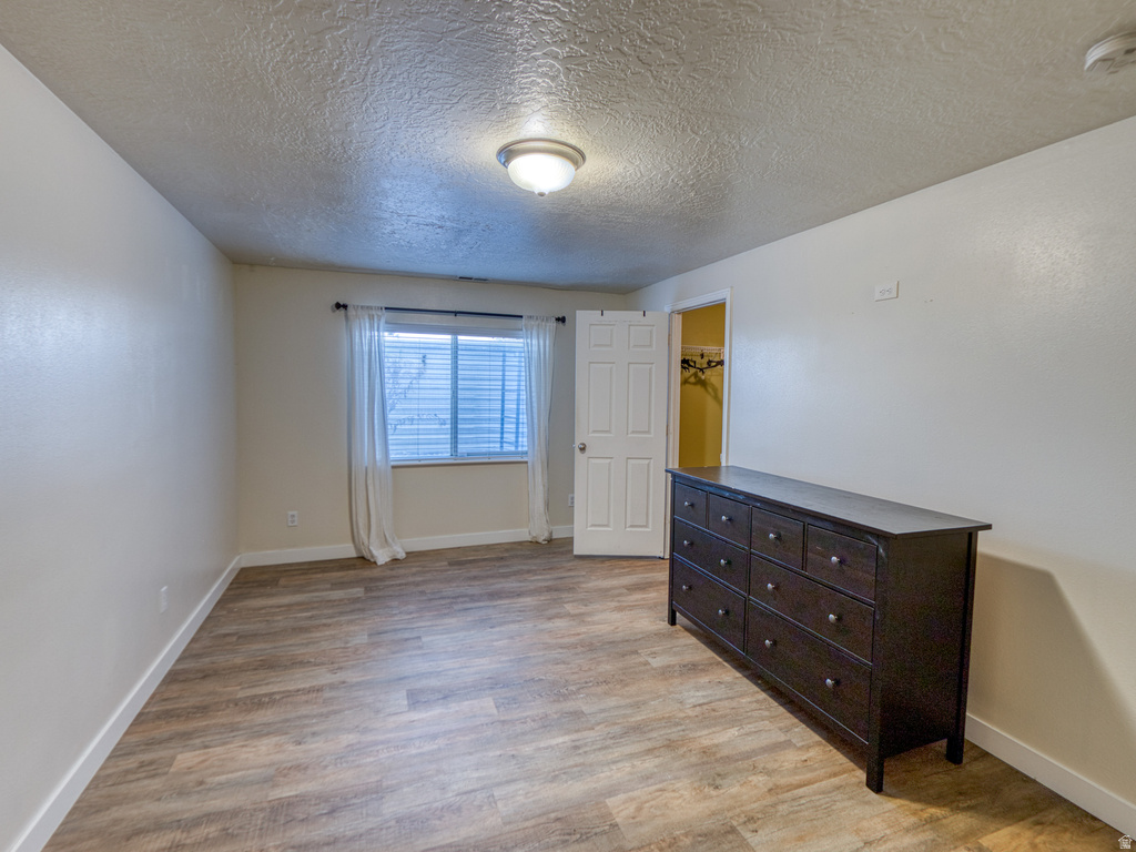 Room featuring wood-finish flooring, neutral wall tones, and a window with blinds and sheer curtains