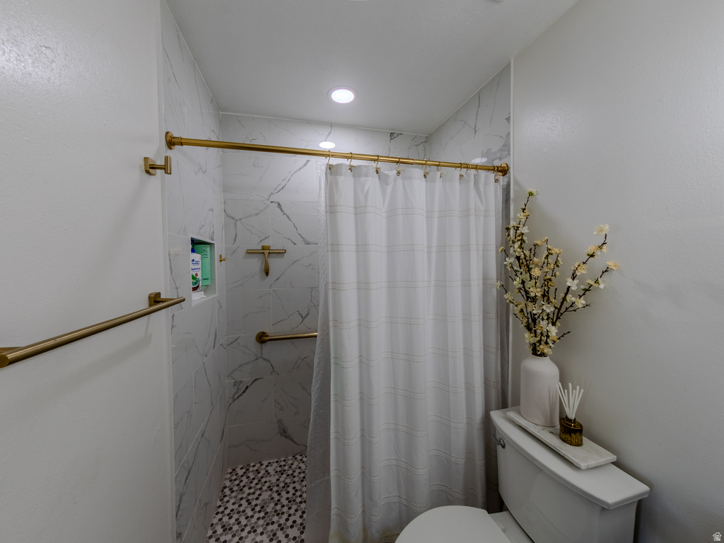 Shower stall featuring white marble-look tile walls, a mosaic pebble floor, and matte gold fixtures