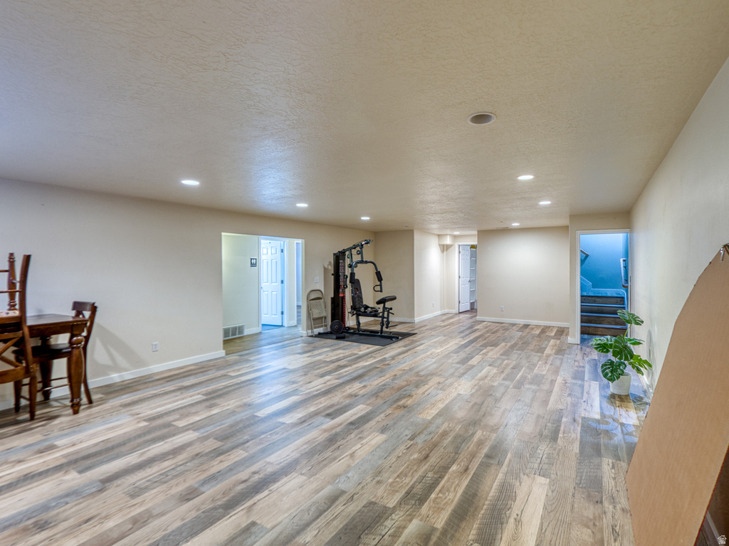 Spacious lower-level room featuring wood-finish flooring, recessed lighting, neutral wall tones, and multiple doorways