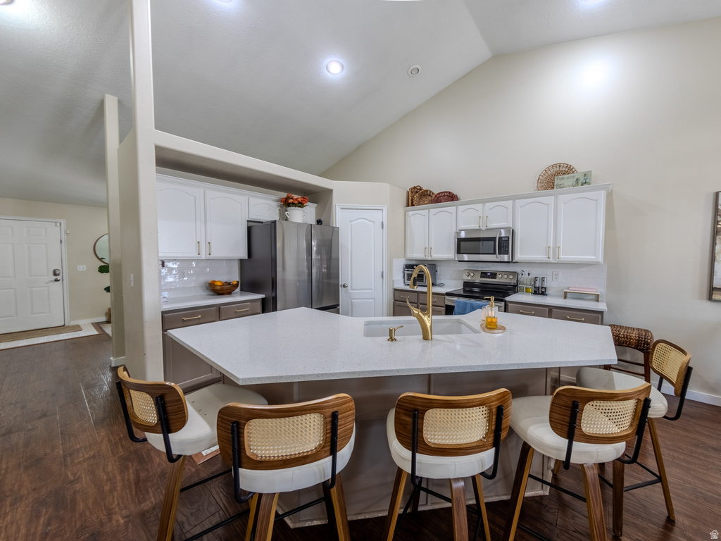 Kitchen with a vaulted ceiling, wood-finish flooring, white cabinetry, stainless steel appliances, and a central island with a gold-tone faucet