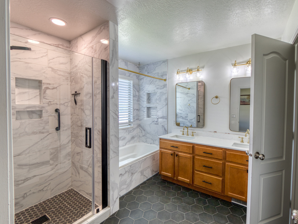 Bathroom featuring a walk-in shower with built-in niches and black hexagonal tile flooring, a built-in bathtub with marble-look tile surround, a double vanity with wood cabinetry and white countertop, and gold-finish fixtures and lighting