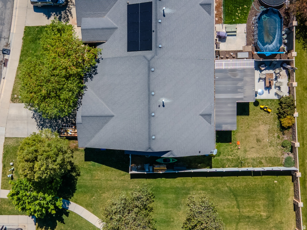 Overhead property view featuring a shingled roofline, solar panel array, covered patio, concrete patio, and fenced backyard with an above-ground pool