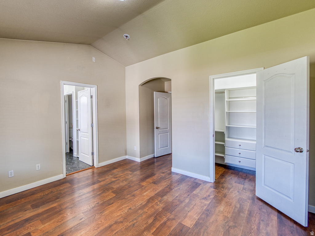 Spacious room featuring wood-finish flooring, vaulted ceiling, built-in closet organization system, and an arched doorway