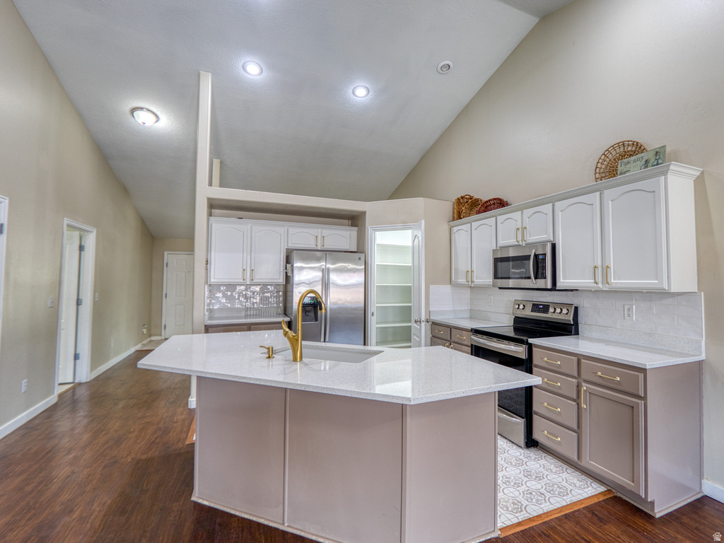 Spacious kitchen featuring a central island with a quartz countertop and integrated sink, stainless steel appliances, white upper cabinetry, and contrasting lower cabinetry
