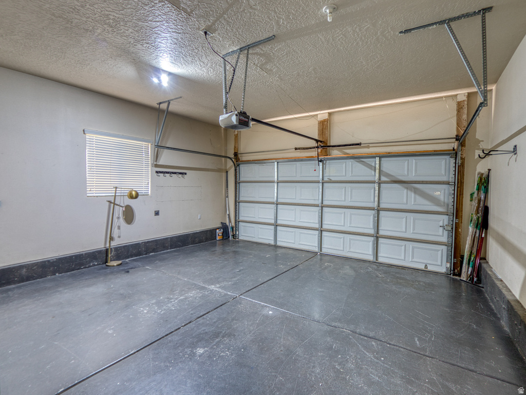 Spacious garage featuring a sectional garage door with automatic opener, concrete flooring, and an elevated window with horizontal blinds