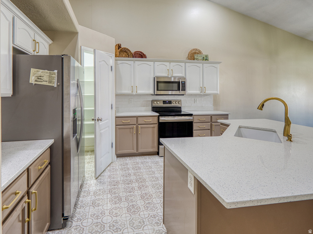 Kitchen featuring a gold-tone faucet, white countertops, built-in stainless steel appliances, and patterned floor tile