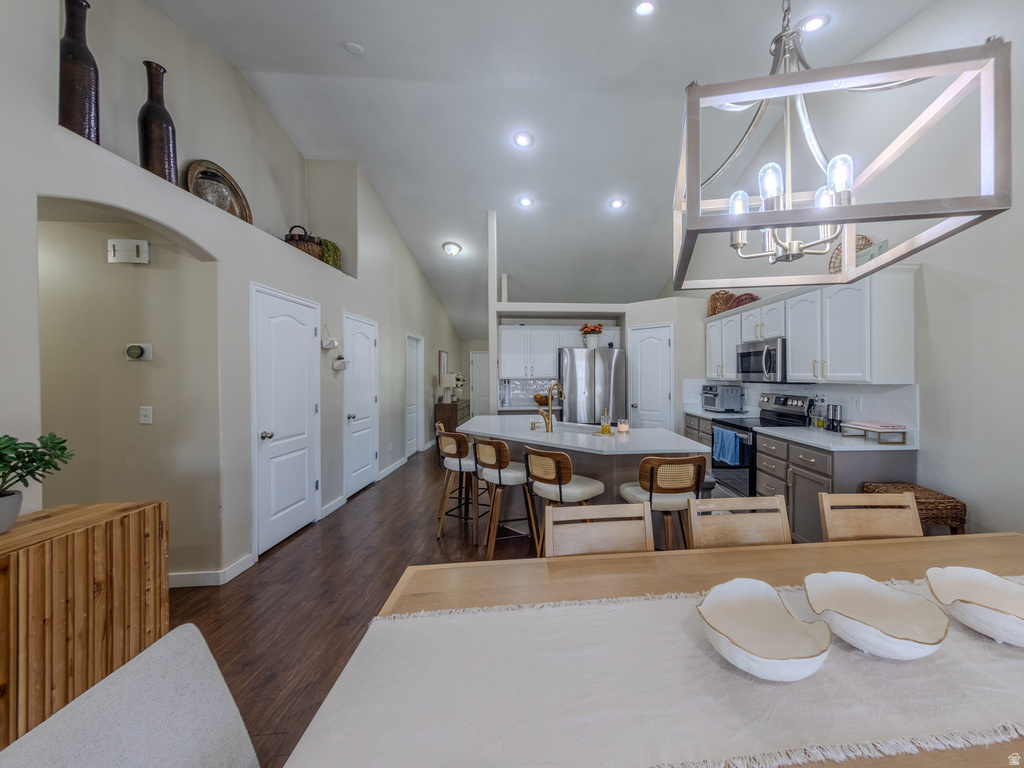 Open-concept kitchen and living area featuring high vaulted ceilings, recessed lighting, wood-finish flooring, a contemporary chandelier, and a kitchen island with seating