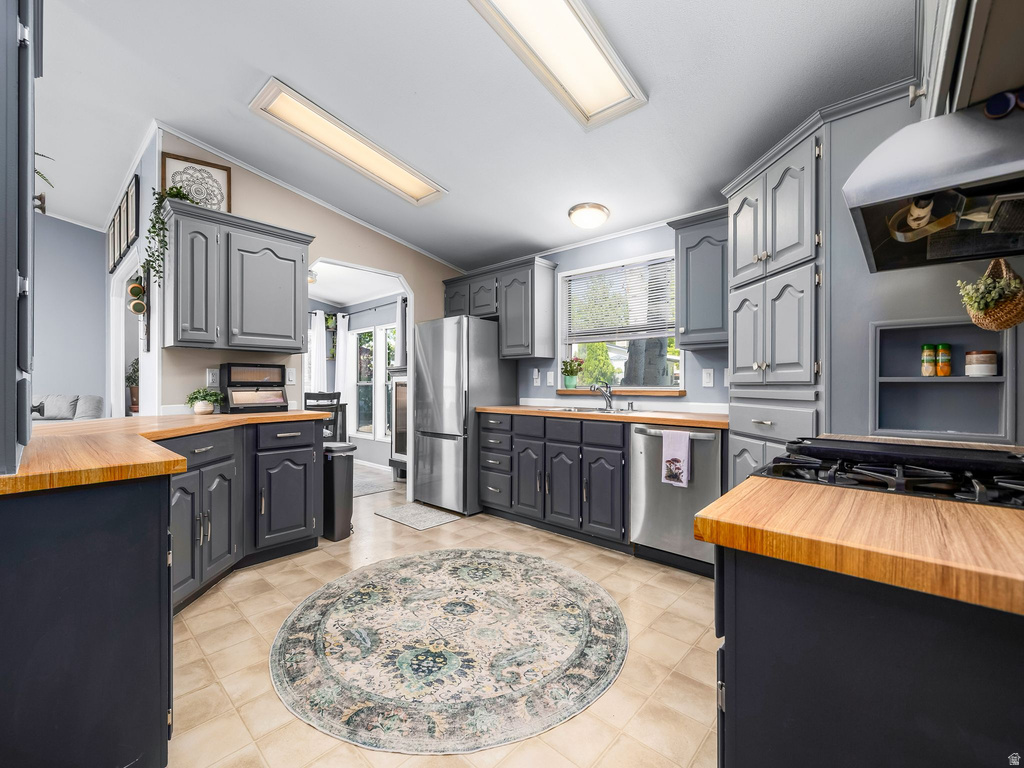 Kitchen featuring wood-finish countertops, stainless steel appliances, abundant cabinetry in a two-tone finish, and tile flooring