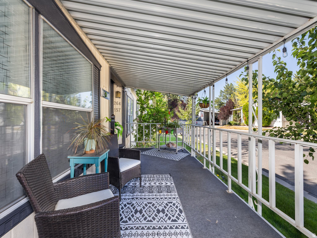 Covered porch with a textured overhead awning, white metal railing, and exterior wall sconce