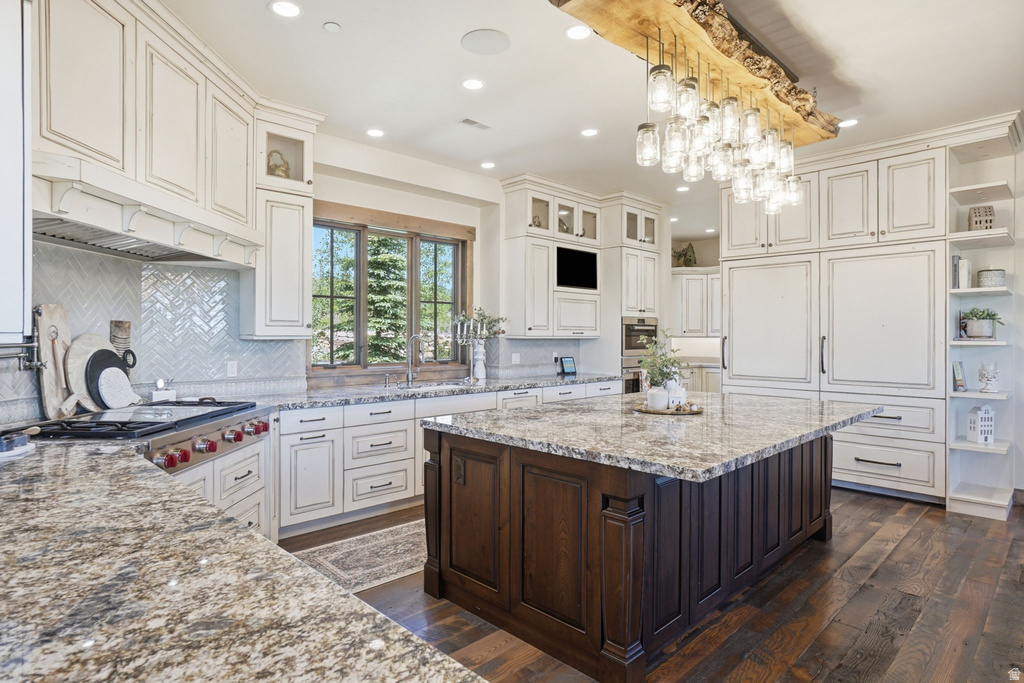 Gourmet kitchen featuring a large central island with a stone countertop, white cabinetry with dark hardware, a herringbone tile backsplash, and dark wood-finish flooring