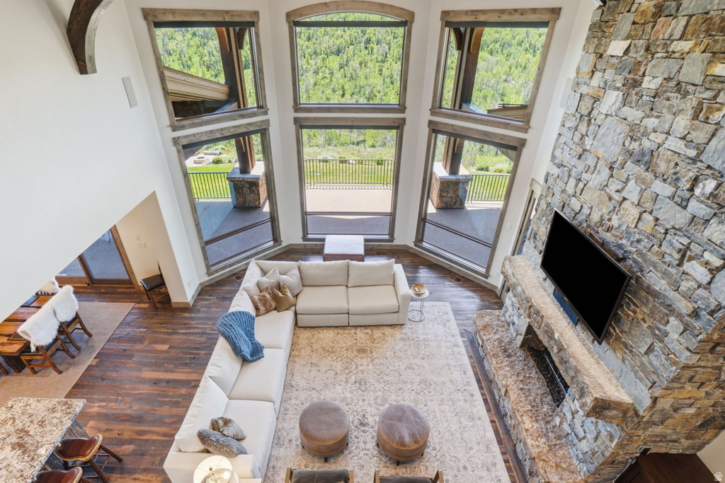 Vaulted living space with a floor-to-ceiling stone fireplace, large picture windows, wood-finish flooring, and exposed ceiling beams