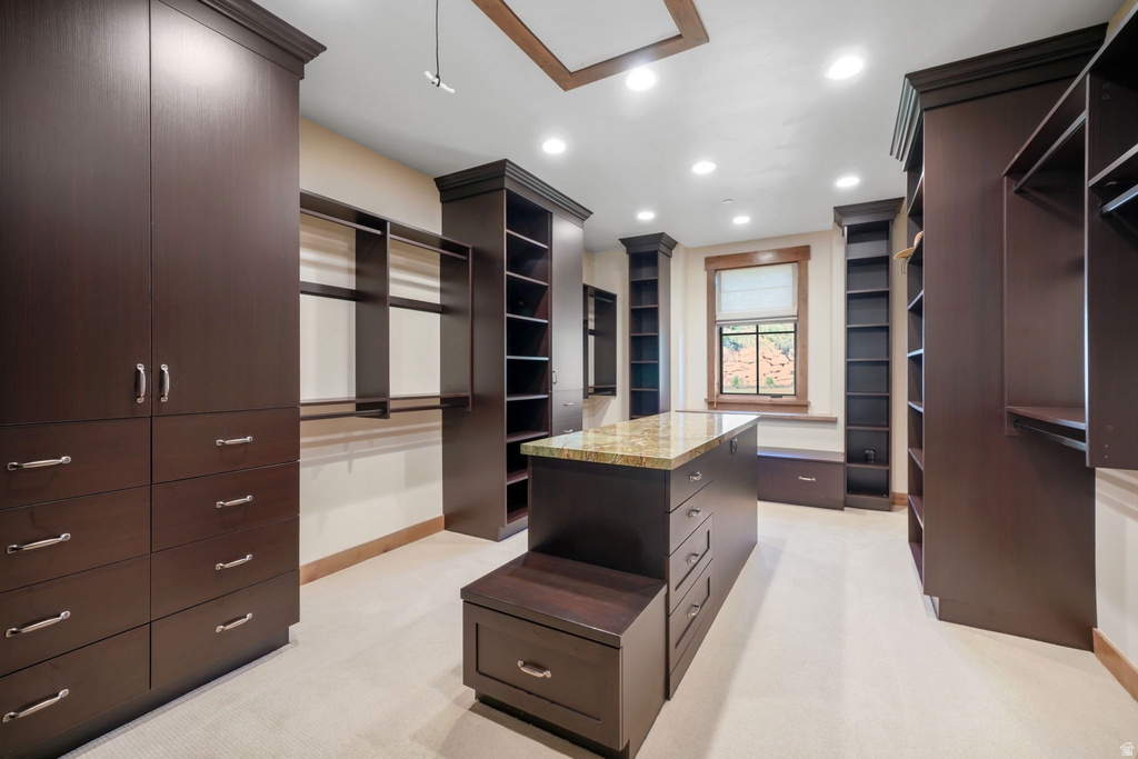 Custom closet system featuring dark wood-finish cabinetry, a central island with a stone countertop, and recessed lighting