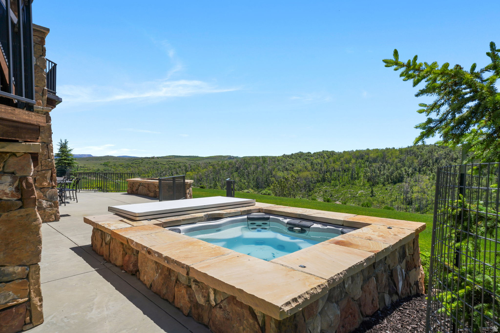 Outdoor spa with stone surround, concrete patio, and distant tree-lined hills