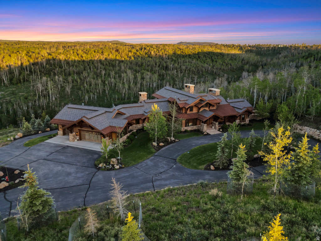 Mountain estate featuring extensive natural wood and stone elements, multiple gables, a multi-car garage, and a winding paved driveway