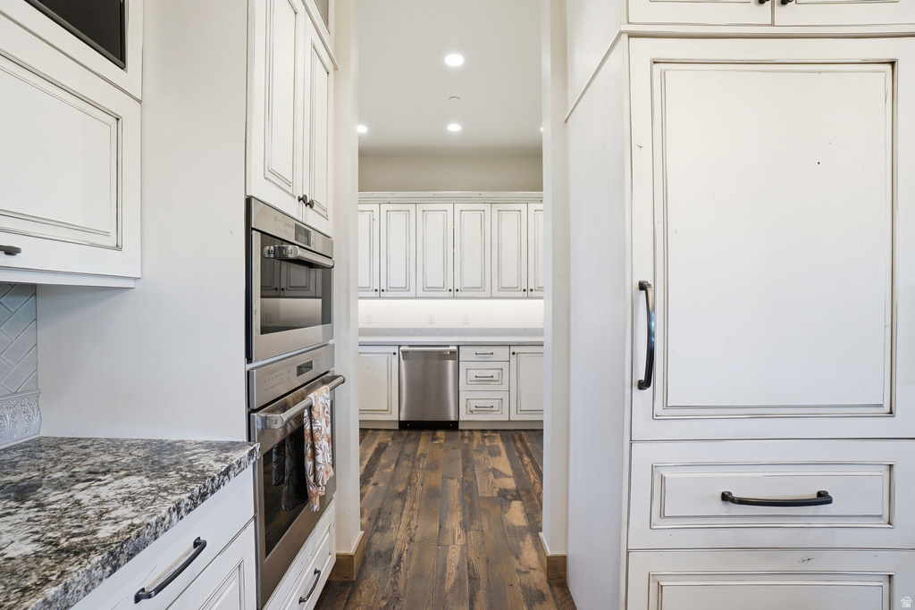 Gourmet kitchen featuring a built-in double oven, paneled refrigerator, white cabinetry with dark hardware, granite-look countertops, and wood-finish flooring