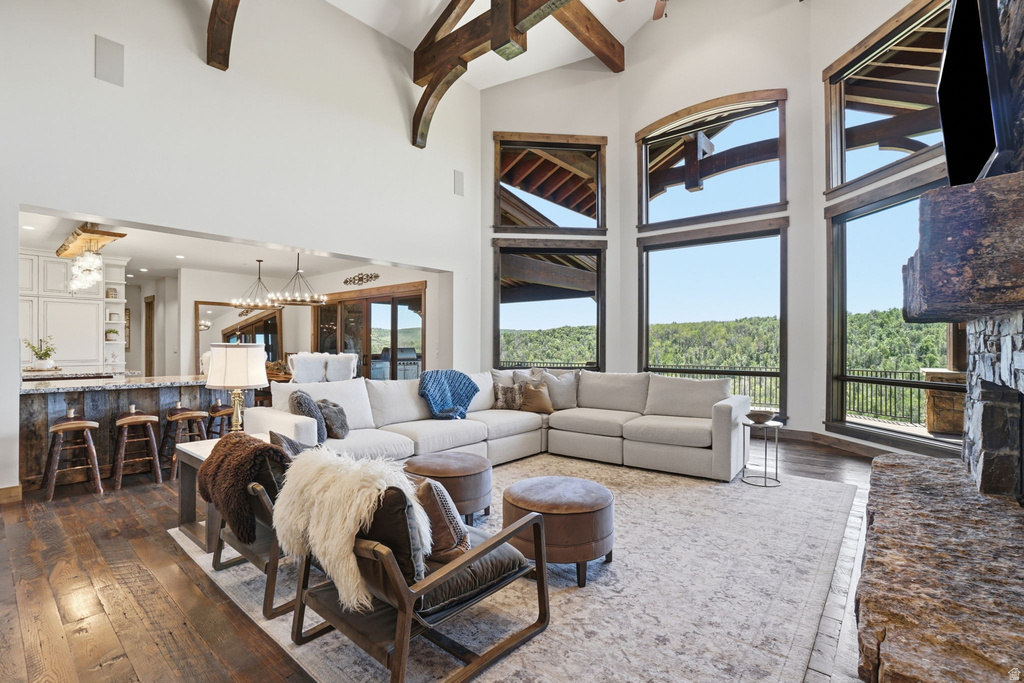Open-concept living space featuring high vaulted ceilings with exposed wood beams, expansive windows, a stone-clad fireplace, and wide-plank wood-finish flooring