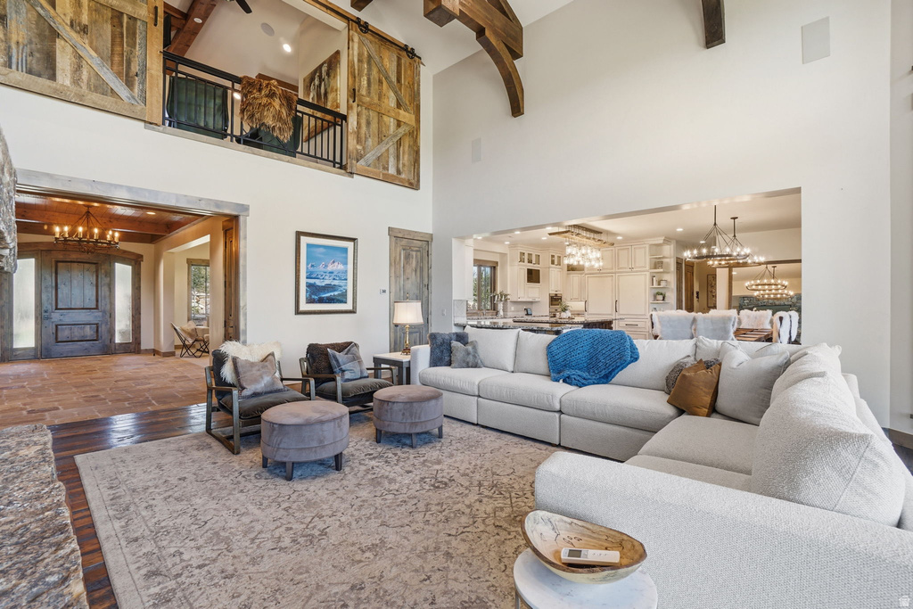 Spacious living area featuring high ceilings with exposed wood beams, a second-story balcony with rustic barn doors, and an open layout to the kitchen and dining areas