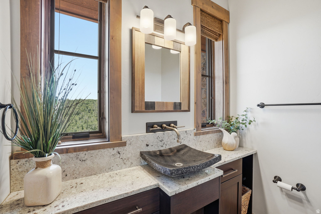 Bathroom vanity featuring a vessel sink, a wall-mounted faucet, and a stone-finish countertop