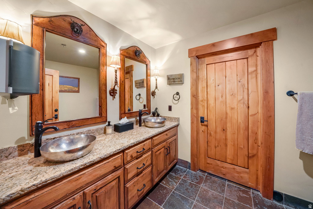 Double vanity with vessel sinks, granite countertops, wood-finish cabinetry, wood-framed mirrors, and tiled flooring