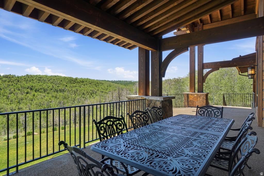 Expansive covered outdoor living space featuring exposed timber beams, a stone-clad support column, and a decorative metal railing