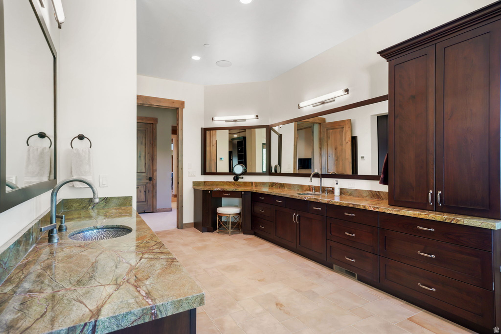 Spacious bathroom featuring two distinct vanity areas, rich wood cabinetry, and multi-toned stone countertops