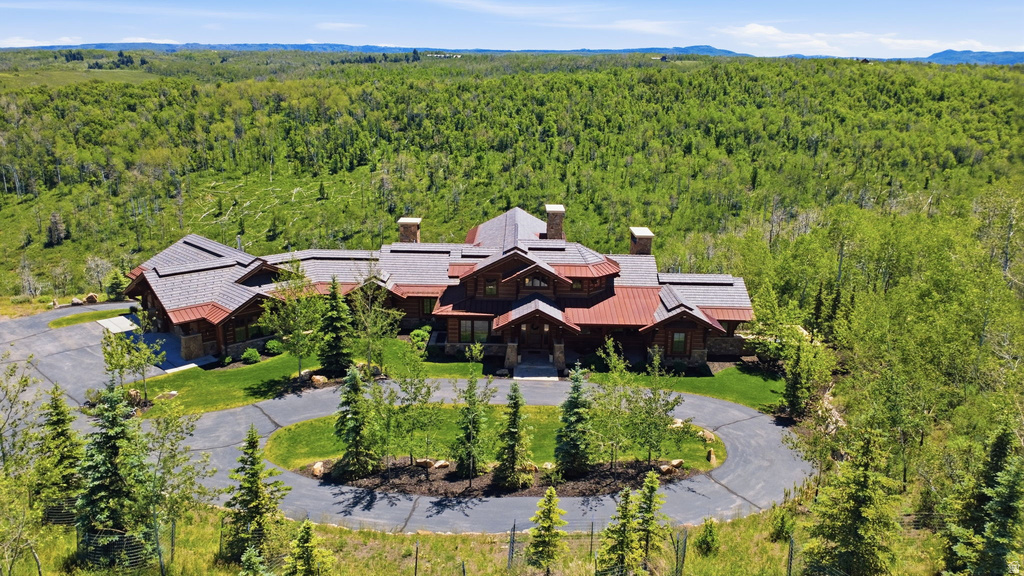 Expansive estate featuring a circular driveway, mature evergreen trees, and a mountain backdrop
