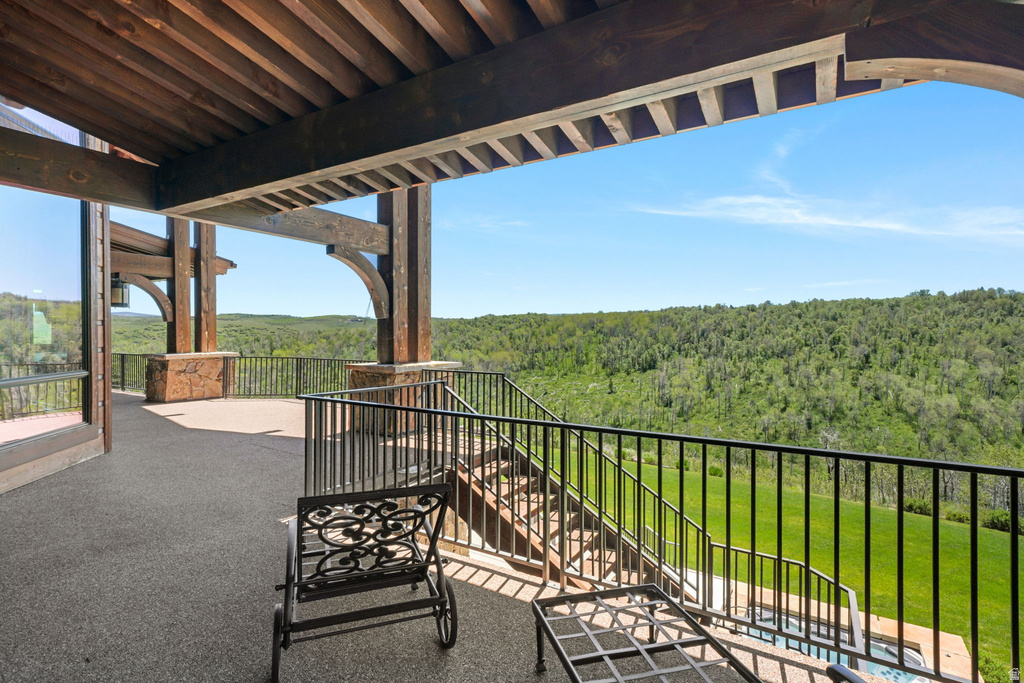 Expansive outdoor patio featuring exposed timber beams, a stone-accented foundation, and black metal railings overlooking a verdant tree line