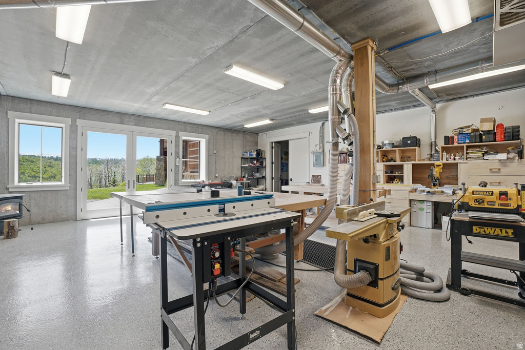 Dedicated workspace featuring an epoxy-coated concrete floor, ample natural light from multiple windows and glass doors, overhead fluorescent lighting, and built-in wood shelving for organized storage