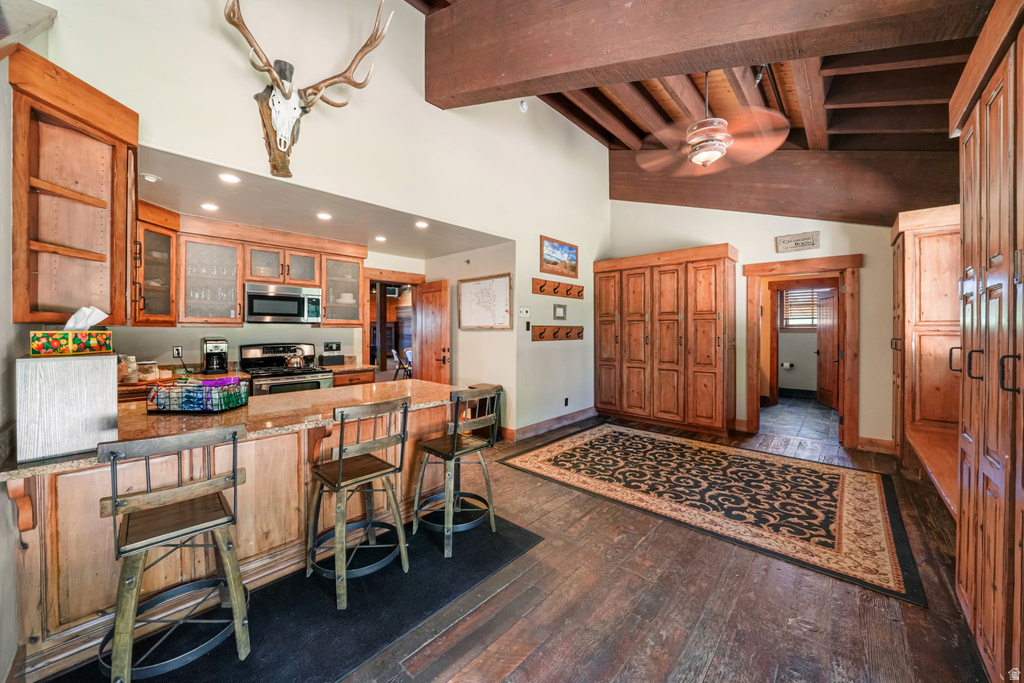Open-concept living space featuring wood-finish flooring, exposed wood beams, and a ceiling fan