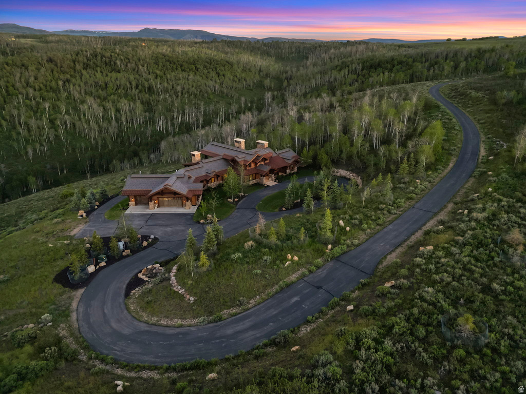 Expansive mountain-side property featuring a multi-level residence with a distinct architectural style, an extensive paved driveway, and surrounding natural landscaping