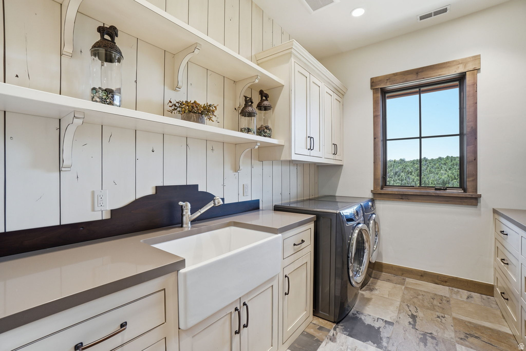 Utility room featuring a farmhouse sink, light cabinetry, and an integrated washer and dryer