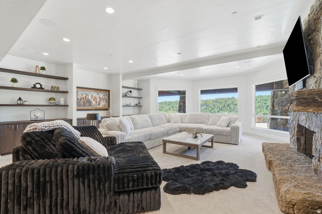 Spacious living area featuring a stone fireplace, multiple windows with a wooded backdrop, recessed lighting, and built-in shelving