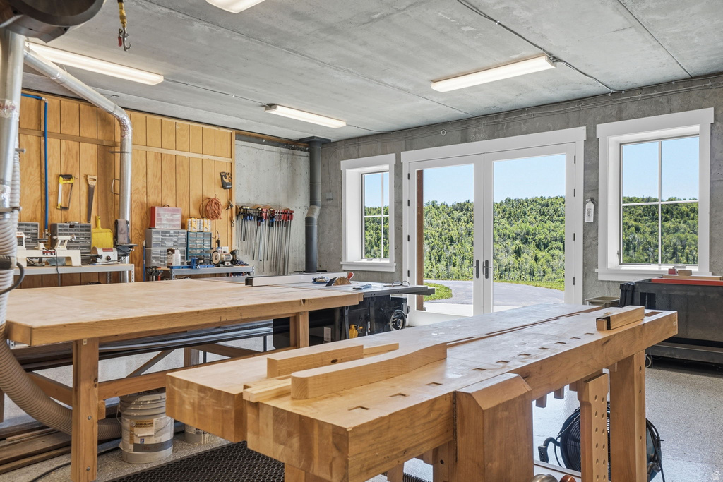 Spacious workshop with concrete walls and ceiling, two large wood workbenches, and wood-finish flooring