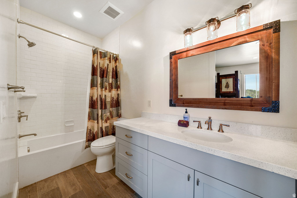 Bathroom featuring wood-finish flooring, a white subway tile shower surround, and a light gray vanity with a light-toned countertop