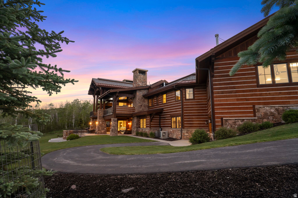 Log home exterior featuring stone accents, multiple large windows, a stone chimney, and a paved circular driveway