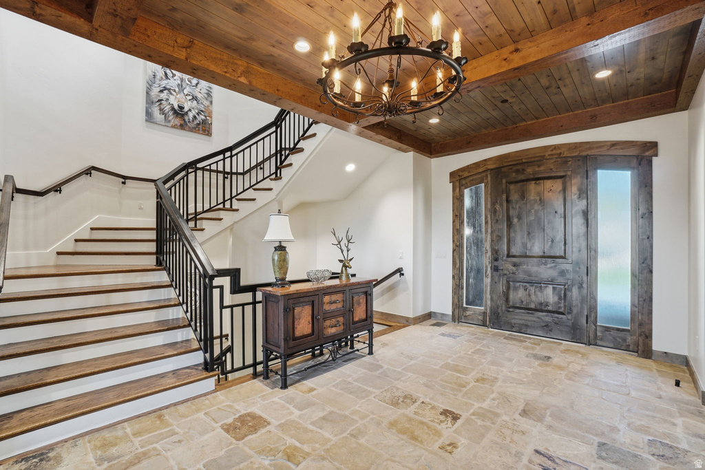 Grand entryway featuring a large wood-finish door with sidelights, stone tile flooring, and a wood-paneled ceiling with exposed beams