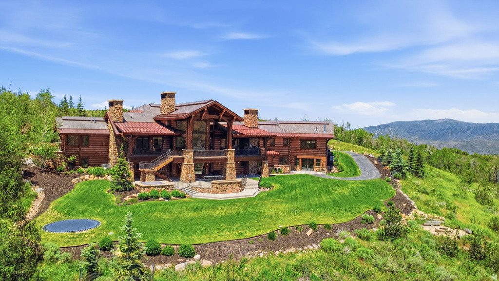 Expansive log home with a red metal roof, multiple stone chimneys, and a stone-clad foundation