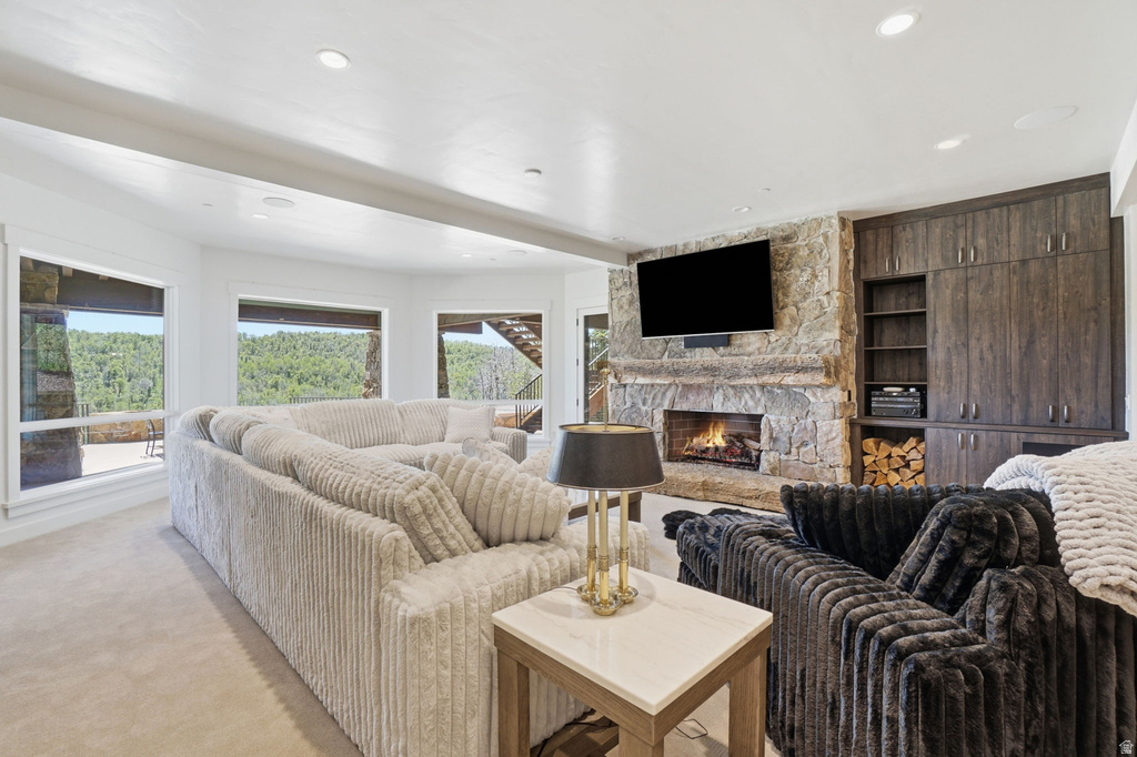 Living area featuring a stone-clad fireplace and hearth, recessed lighting, built-in cabinetry, large windows, and carpet flooring