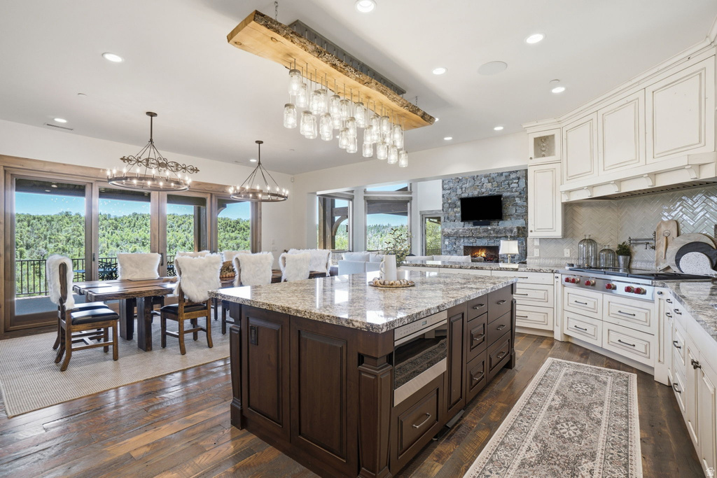 Spacious open-concept kitchen and dining area featuring wood-finish flooring, a large kitchen island with a stone countertop, white cabinetry, a built-in range, and expansive glass doors opening to a balcony