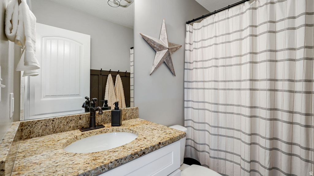 Bathroom featuring a speckled stone countertop, white oval undermount sink, dark bronze-finish faucet, and a white vanity cabinet
