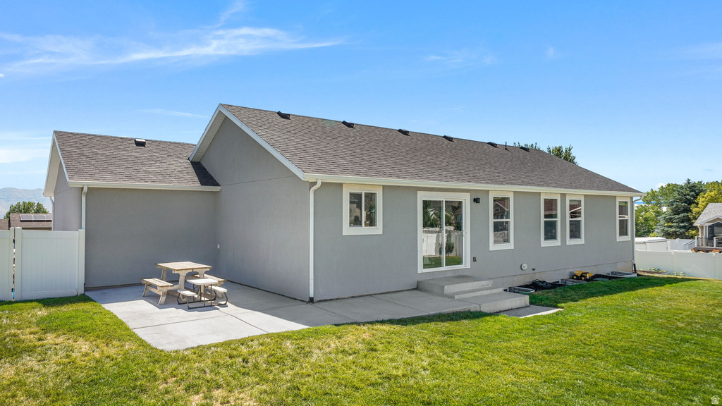 Expansive rear lawn featuring a concrete patio, sliding glass door entry, multiple windows with white trim, and a partial white privacy fence