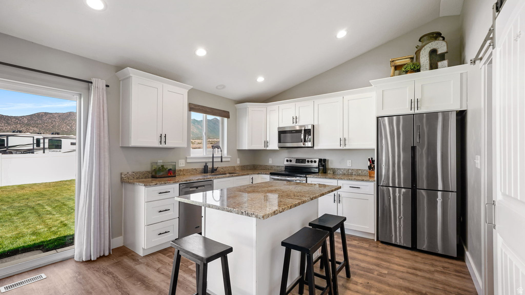 Kitchen featuring wood-finish flooring, white cabinetry, granite countertops, stainless steel appliances, and a central island with bar seating