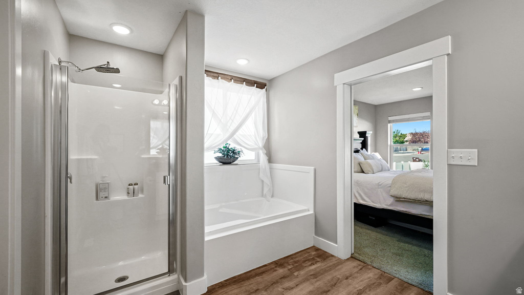 Spacious bathroom featuring a glass-enclosed shower, built-in bathtub, recessed lighting, and wood-finish flooring
