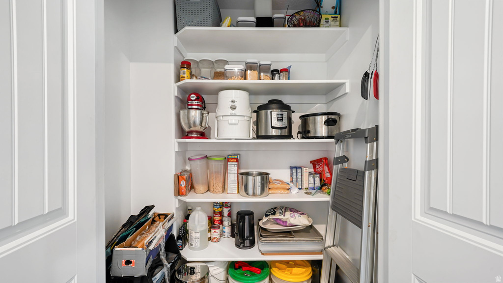 Pantry featuring multiple white shelving units, white walls, and a white paneled door