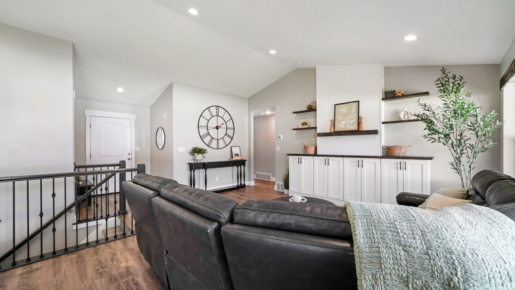 Open-concept living space featuring vaulted ceilings, wood-finish flooring, recessed lighting, built-in cabinetry with a dark countertop, and floating shelves