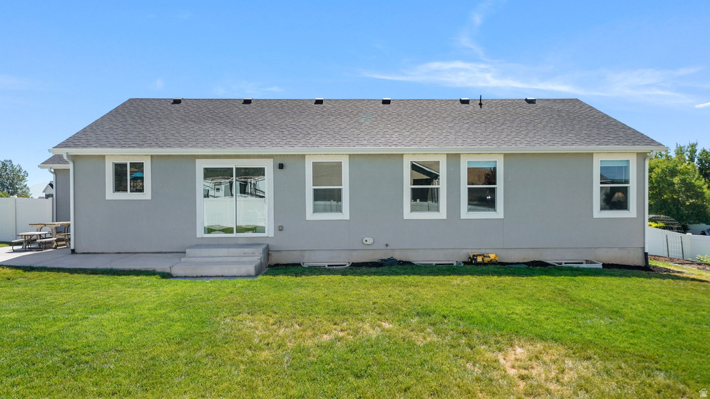 Expansive rear exterior featuring a concrete patio, sliding glass door, multiple windows with white trim, and a gray shingle roof