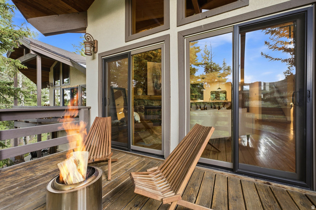 Expansive wood-plank deck with a built-in railing, featuring large sliding glass doors, a decorative exterior light fixture, and a partial glimpse of an interior space through the glass