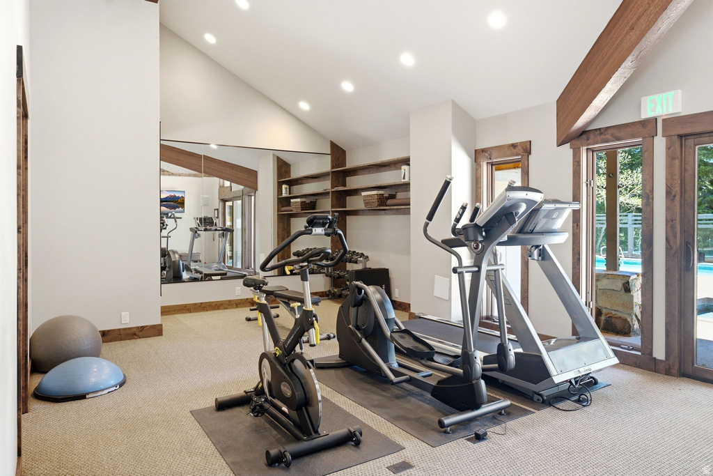 Dedicated exercise room featuring a vaulted ceiling with recessed lighting, exposed wood beams, and a large wall-mounted mirror