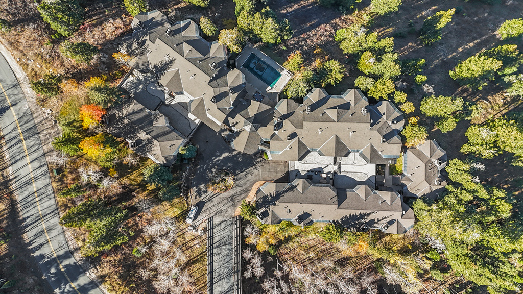 Expansive property featuring a multi-level roofline, extensive paved driveways, a swimming pool, and surrounding mature trees
